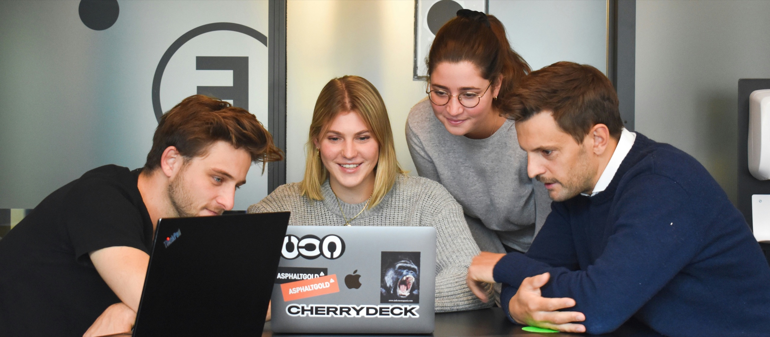 Four coworkers collaborating around laptops in a modern office